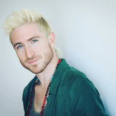 a man with blonde hair and blue eyes wearing a green shirt is looking at the camera