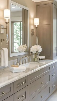 a large bathroom with two sinks and mirrors on both sides of the countertop, along with white flowers in vases