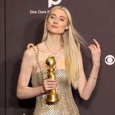 a blonde woman holding an award in her right hand and wearing a gold dress with sequins on it