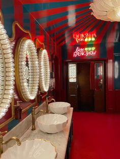 two sinks in a red and blue bathroom with lights on the wall above them, along with large round mirrors