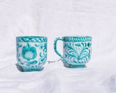 two blue and white coffee mugs sitting side by side on a white cloth background