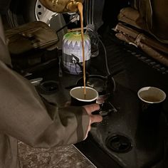 a person pouring something into a cup on top of a stove in the back of a car