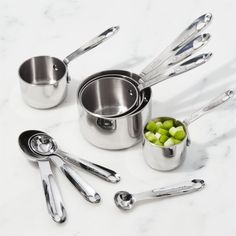 stainless steel pots and pans with green vegetables in them on a marble countertop