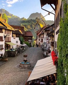 an old town with mountains in the background and people sitting at tables under umbrellas