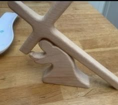 a wooden cross sitting on top of a table next to a white bowl and spoon