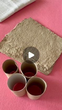 three empty cups sitting on top of a pink surface next to a piece of paper