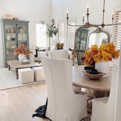 a dining room table with white chairs and flowers in vases on the end tables