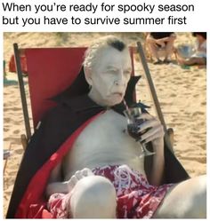 an older man in a red and black cape drinking from a bottle while sitting on a beach chair