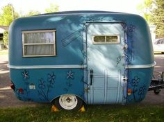 an old blue trailer with flowers painted on it's side parked in the grass