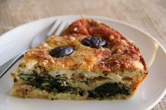 a slice of quiche with olives and spinach is on a white plate