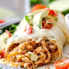 an enchilada on a plate with tomatoes and lettuce