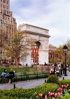 people are sitting on benches in the middle of a park with tall buildings behind them