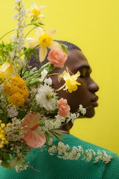 a woman with flowers on her head in front of a yellow wall and green sweater