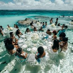 a group of people sitting around a round table in the water at a beach wedding