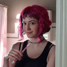 a woman with pink hair is holding a toothbrush in her hand and looking at the camera