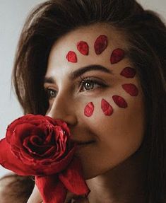 a woman with painted on her face holding a red rose in front of her face