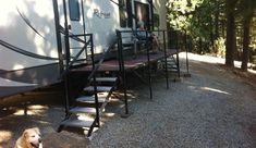 a dog sitting on the ground in front of a trailer with stairs leading up to it