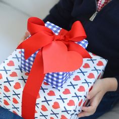 a child holding a wrapped present box with red ribbon and heart cutouts on it