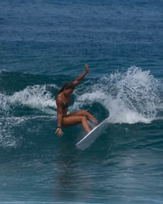 a woman riding a surfboard on top of a wave in the ocean with her arms up