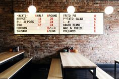 two large menu boards mounted on the wall in a restaurant with wooden benches and tables