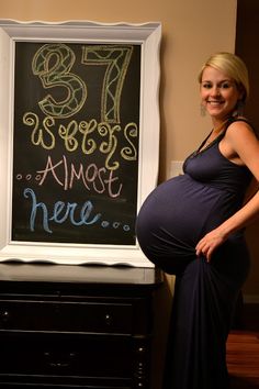 a pregnant woman standing in front of a chalkboard