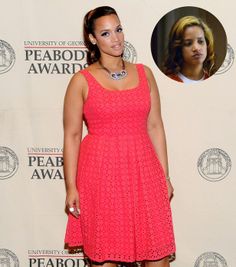 a woman standing in front of a white wall wearing a pink dress and black heels