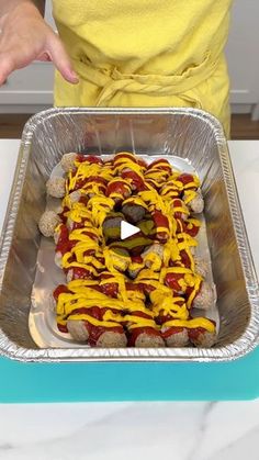 a person holding a pan filled with hotdogs covered in mustard and ketchup