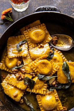 a skillet filled with ravioli and spinach covered in cheese sauce next to flowers