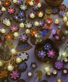 many candles are lit on the table with flowers and leaves around them in different colors