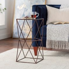 a small side table with a cup on it in front of a blue couch and white rug