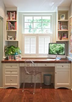 a desk with a computer on top of it in front of a window and bookshelves