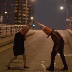 two people standing on the side of a road with traffic cones over their heads,