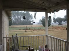 an empty rocking chair on the front porch overlooking a field and cornfield in the distance