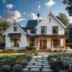 a white house with lots of windows and plants on the front lawn, surrounded by greenery