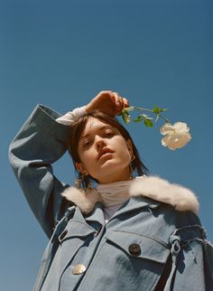 a woman holding a flower up to her head while wearing a blue jacket and fur collar