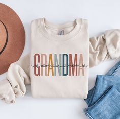 a white shirt with the word grandma printed on it next to jeans and a hat