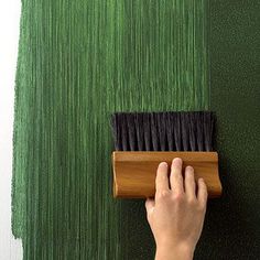 a person using a brush to paint a wall with green grass on the outside and inside