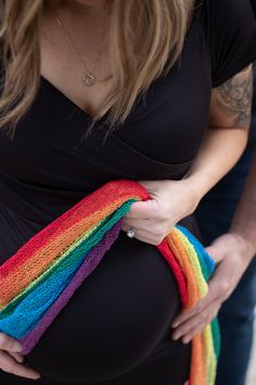 a pregnant woman holding a rainbow colored knitted object in her hands and wearing a black shirt