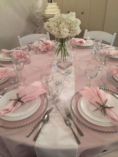 the table is set with silverware and pink napkins, white flowers in vase