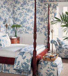 a bedroom with blue and white floral wallpaper, four poster bed, and matching foot stools