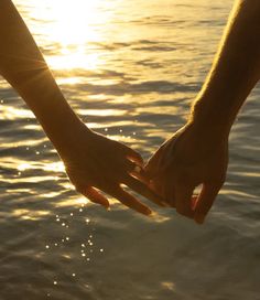 two people holding hands over water with the sun setting in the background and sunlight reflecting on the water