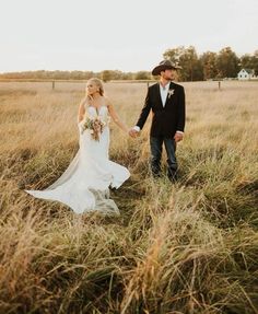 a bride and groom holding hands walking through tall grass