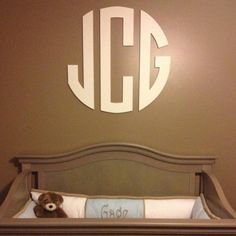 a teddy bear sitting on top of a bed in front of a monogrammed wall