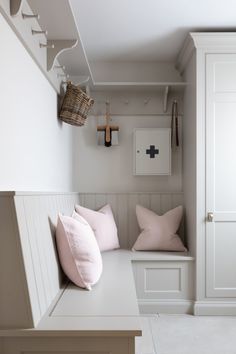 a white bench with two pink pillows on top of it and some hooks hanging from the wall