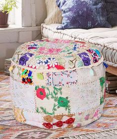 a multicolored patchwork ottoman sits on a rug in front of a window