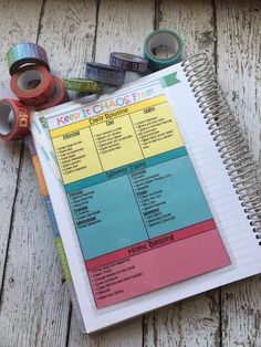 a spiral notebook sitting on top of a wooden table next to some tape and scissors