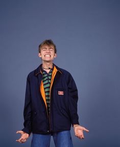 a man with his hands out in front of him, wearing an orange and blue jacket