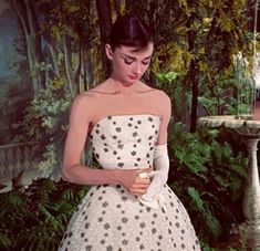 a woman in a polka dot dress standing next to a birdbath and trees