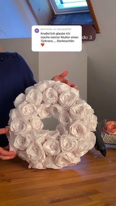 a man holding a wreath made out of rolled up paper flowers on top of a wooden floor