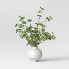 a white vase filled with green leaves on top of a table